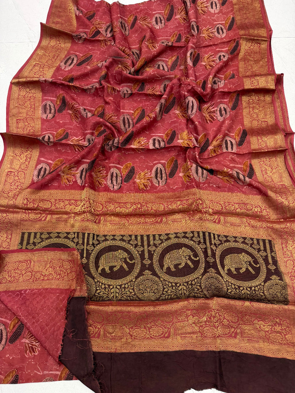 A draped red and gold Banarasi silk saree with intricate zari embroidery, featuring elephant motifs on the border and a matching red fabric piece folded underneath.