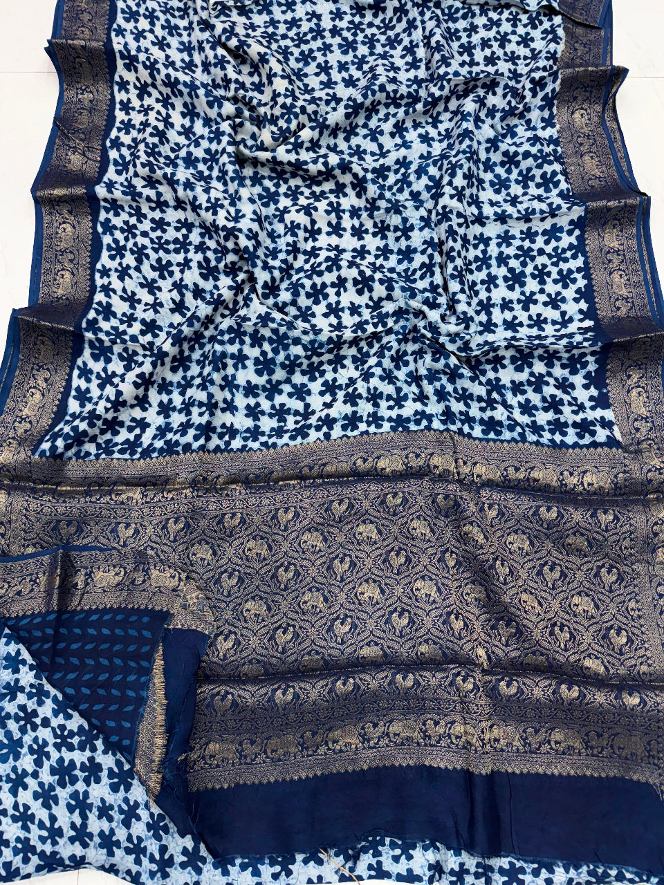 A blue and white printed saree with a wide navy and gold patterned border, laid flat on a white surface.