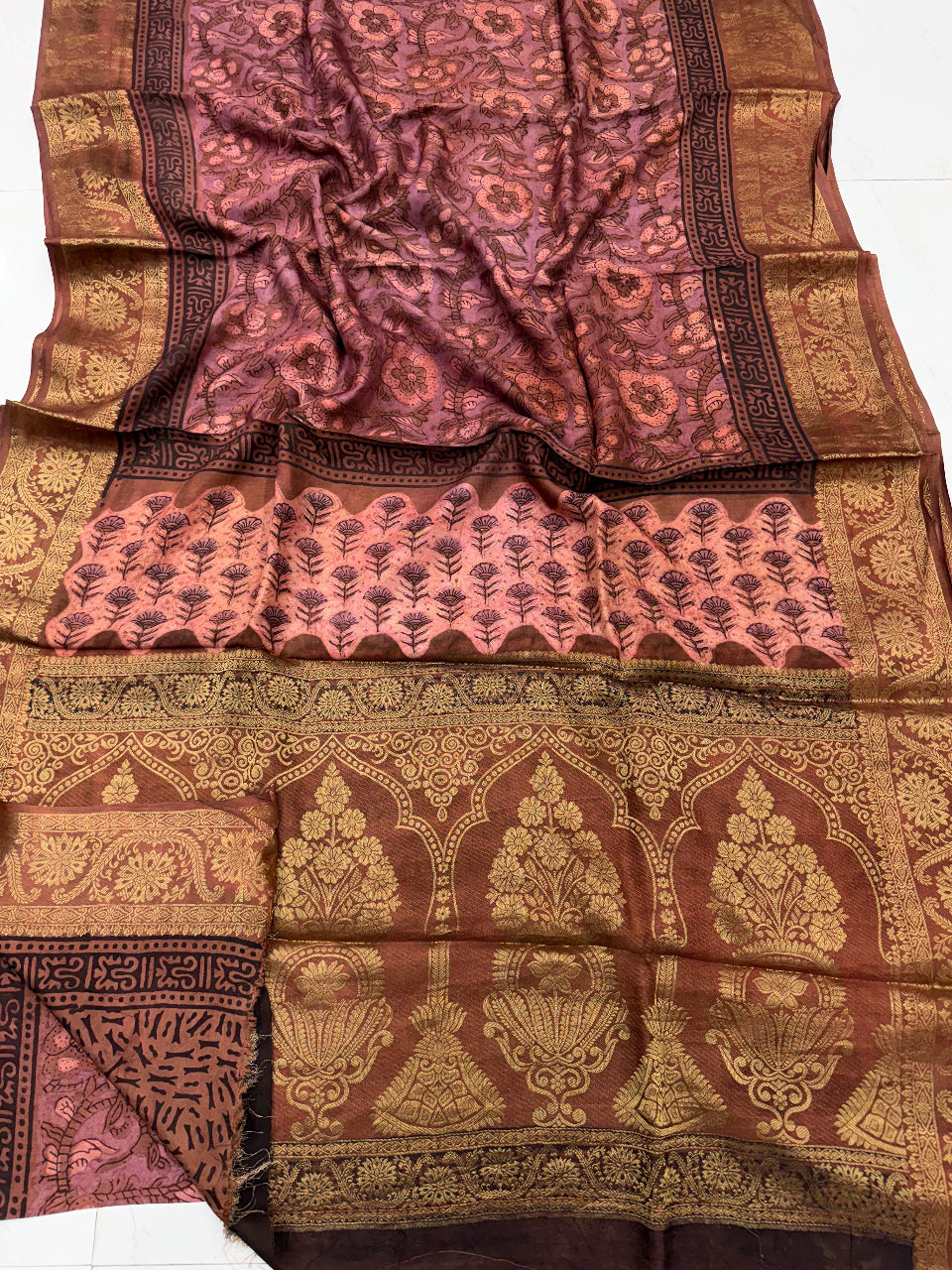 A traditional Indian silk saree with a rich brown and gold zari pattern, featuring a floral body, a pink and gold border, and an ornate arched pallu.