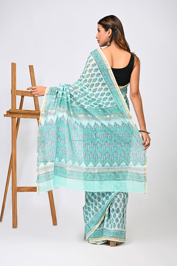 Back view of a woman modeling a light green Sanganeri print Chanderi Silk saree, showcasing its shimmering sheer drape, delicate hand block printed buti motifs, and matching patterned pallu next to a wooden easel.