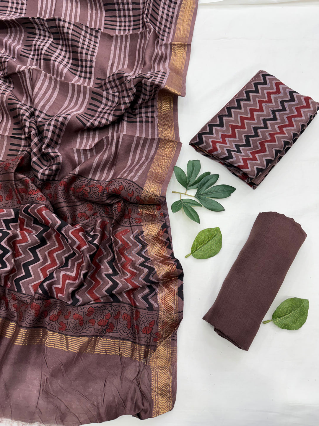Brown and red zig-zag patterned unstitched kurta fabric accented with green leaf styling props