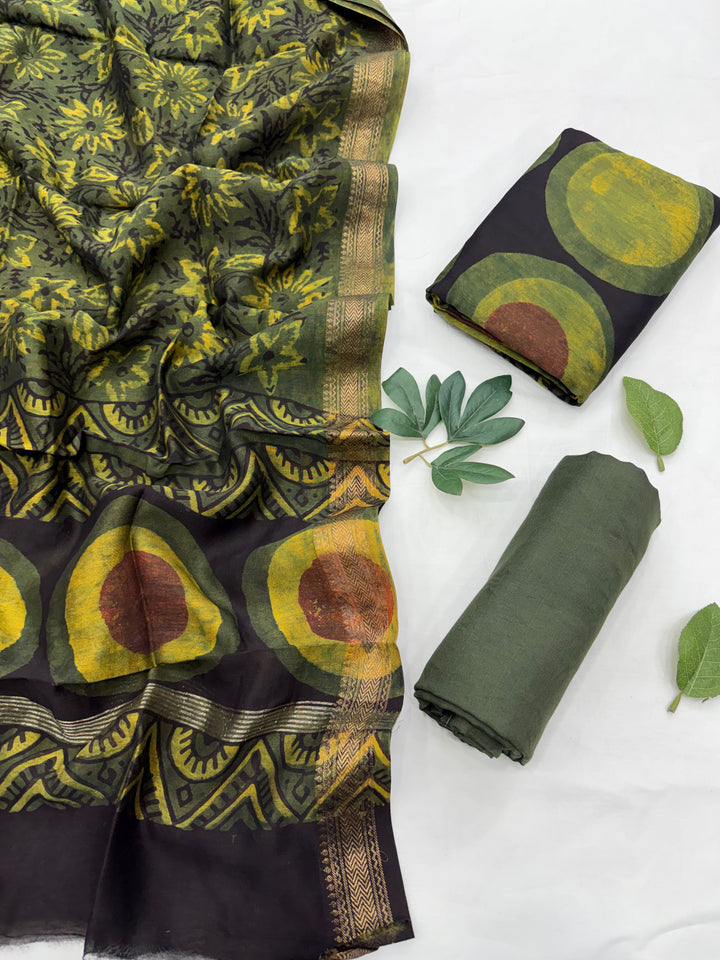 Dark green and black Maheshwari silk unstitched suit set featuring large geometric circle patterns with yellow and red accents, displayed with a patterned dupatta and folded fabric pieces on a white background