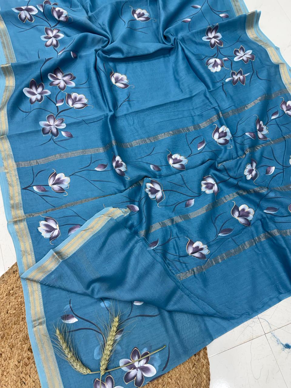 Blue Maheshwari handloom silk saree featuring handpainted white and purple floral patterns with a traditional gold zari border.