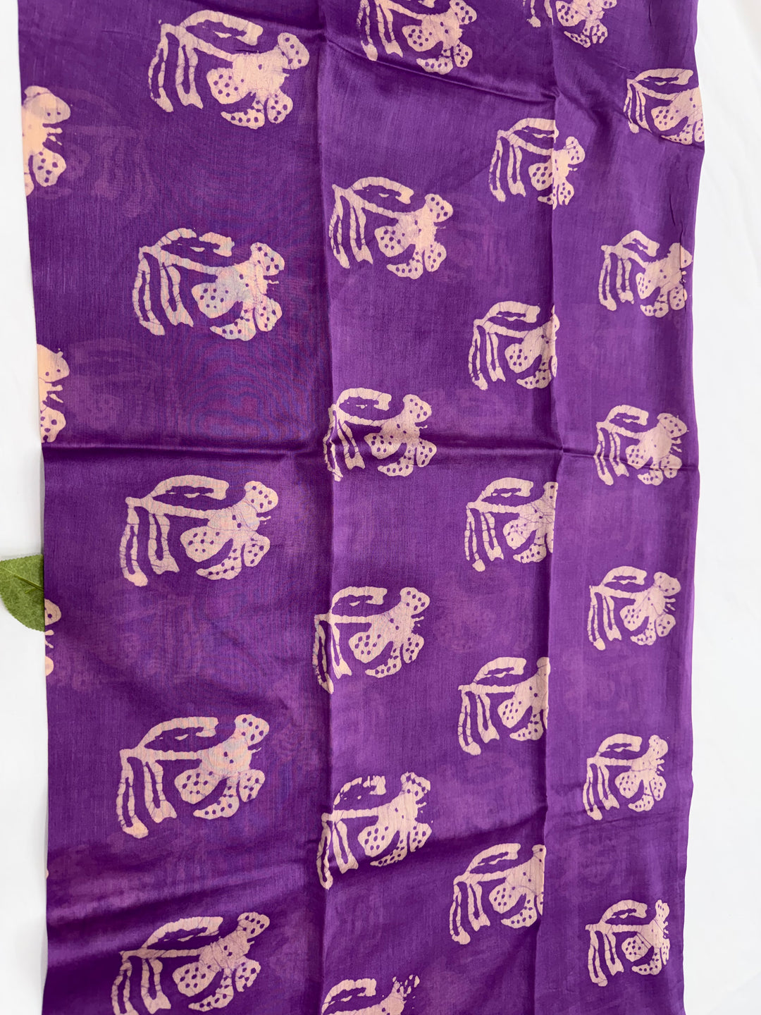 Purple fabric with a repeating block-printed pattern of light beige figures, laid flat against a white background.