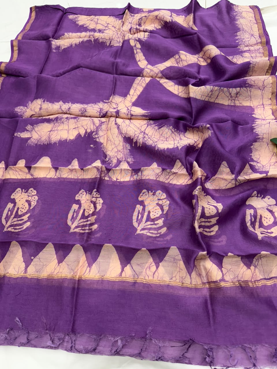A purple silk saree with beige tie-dye (shibori) patterns, featuring large abstract leaf-like designs, a decorative border with frog motifs, and a geometric triangle pattern.