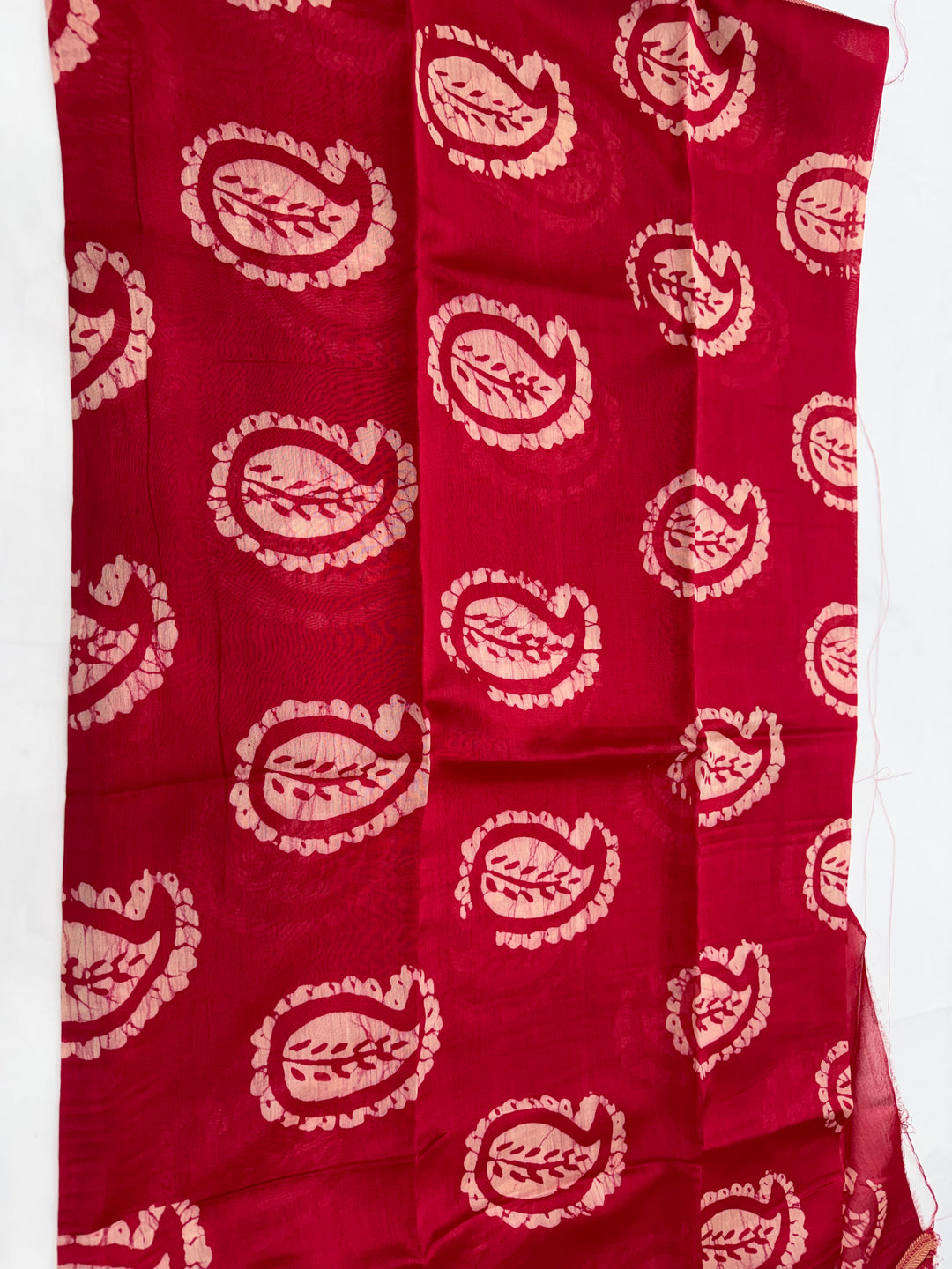 A red fabric, likely a dupatta or scarf, featuring a repeating block-printed paisley pattern in a light beige or cream color.