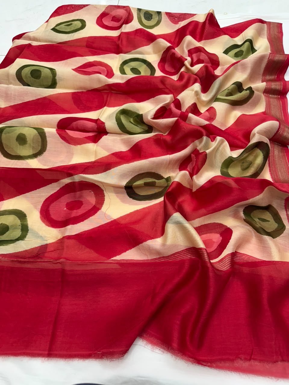 A red and beige patterned scarf with green and pink circular motifs, draped on a white surface.