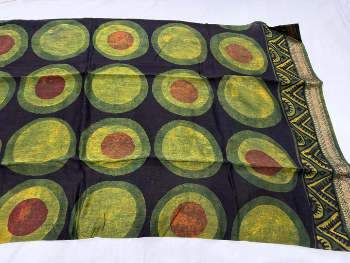 Dark green and black Maheshwari silk unstitched suit set featuring large geometric circle patterns with yellow and red accents, displayed with a patterned dupatta and folded fabric pieces on a white background