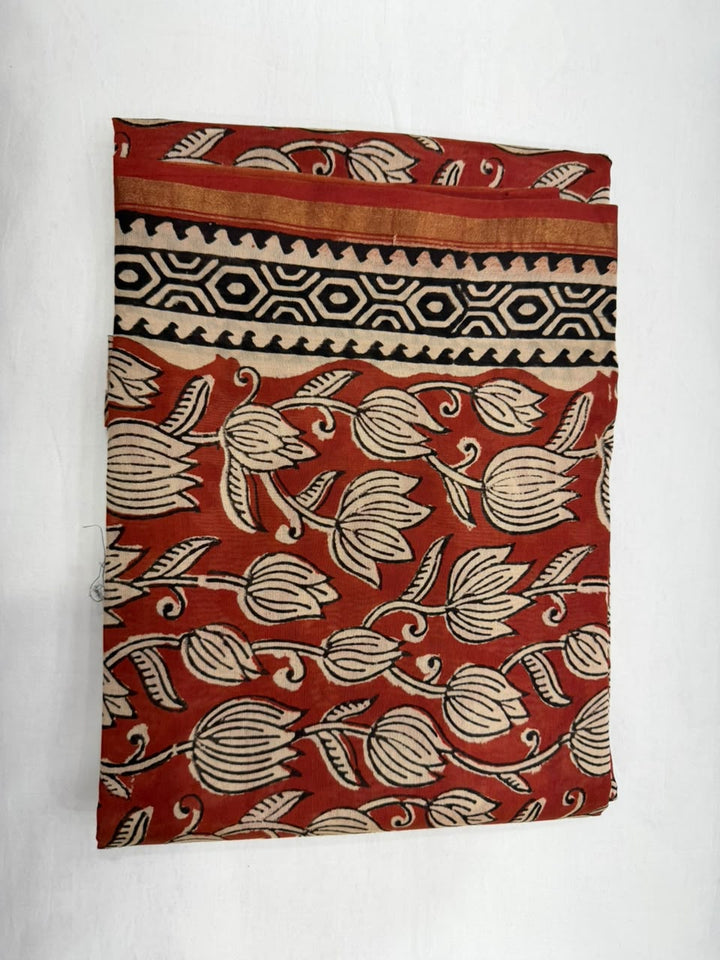 A folded piece of rust-red cotton fabric with a beige floral block print and a black geometric border pattern, displayed against a white background.