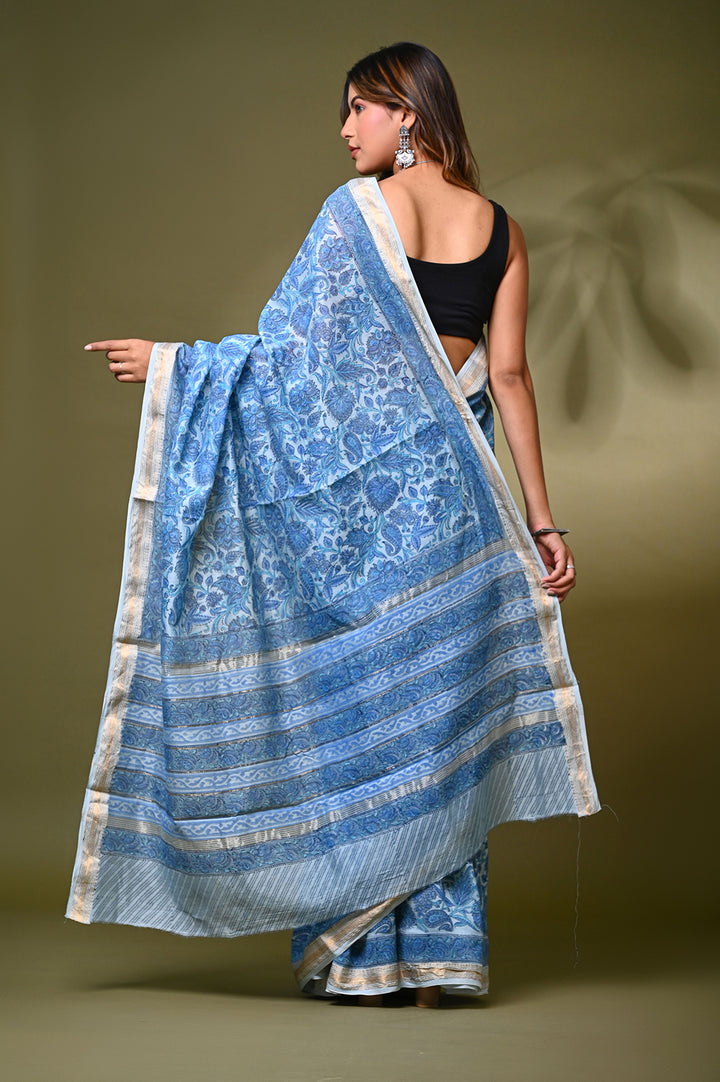 Model wearing a light blue Sanganeri hand-block floral print Maheshwari silk-cotton saree with a classic gold zari border and matching unstitched blouse piece.