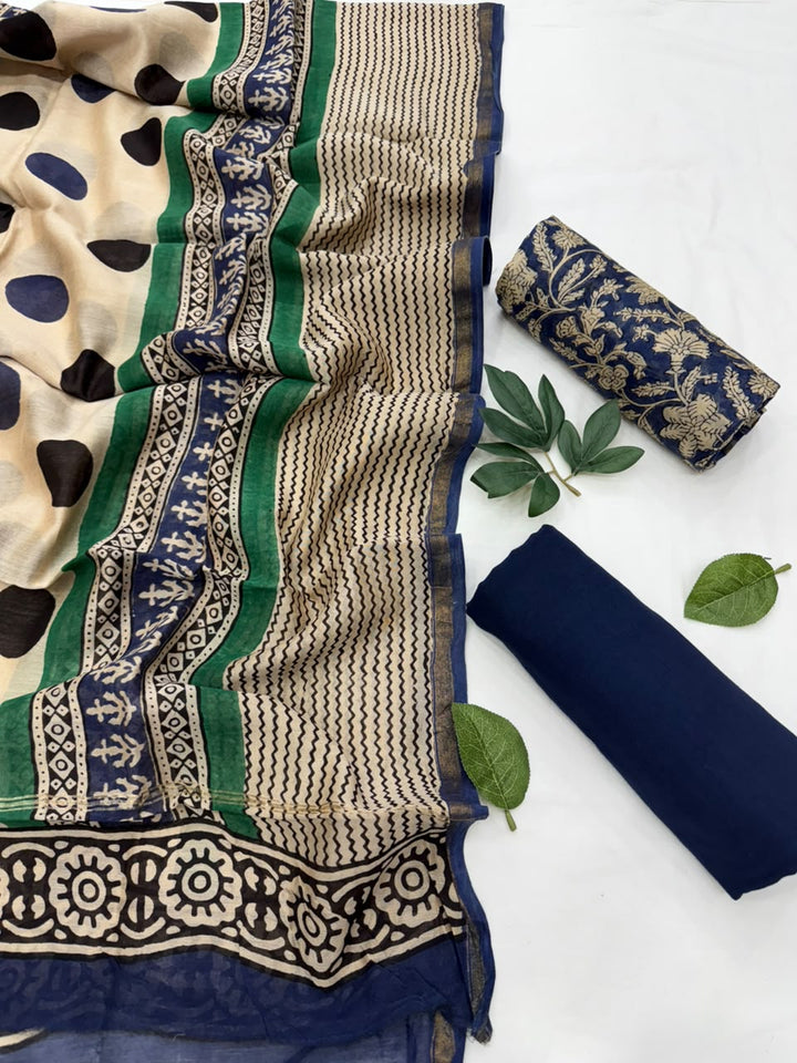 A folded and rolled navy blue fabric set with a beige and navy patterned dupatta featuring green and beige patterned borders, displayed on a white background with decorative green leaves