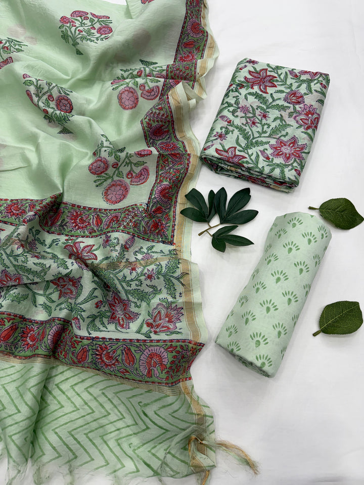 A folded and draped pastel green Chanderi silk suit set featuring delicate floral and geometric block prints in pink, red, and green, displayed against a clean white background.