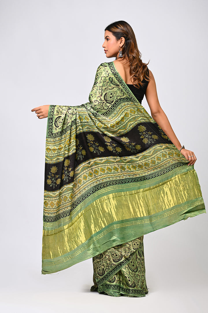 A woman modeling an Ajrakh Vanaspati print Modal Silk saree featuring an elegant designer pallu and a golden Lagdi Patta geometric border.