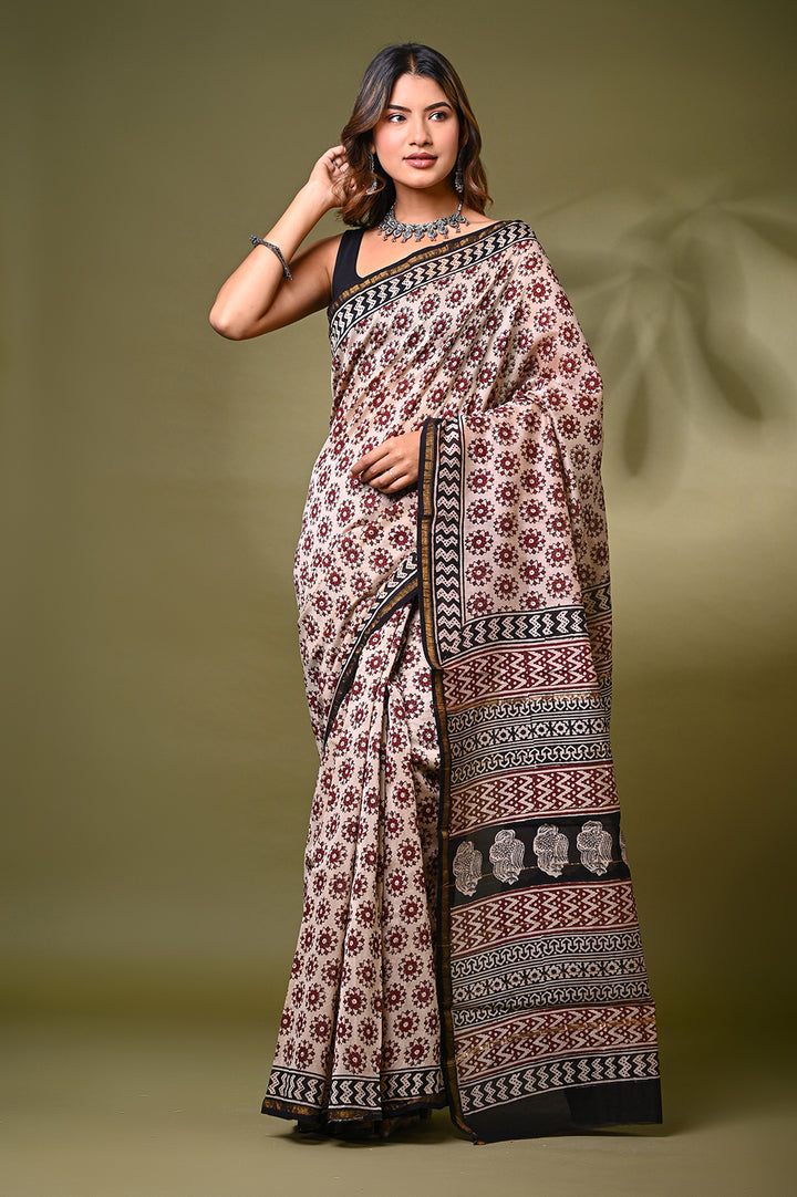 A woman modeling an authentic natural cream Chanderi silk saree with intricate hand block printed Bagru motifs, a patterned border, and an elegant pallu against a muted green background.