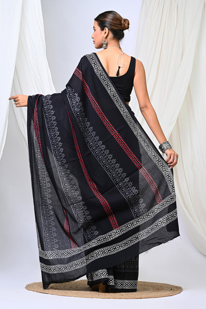 A woman modeling the beautiful designer pallu of a black and white Bagru hand block print mulmul cotton saree with red border detailing.
