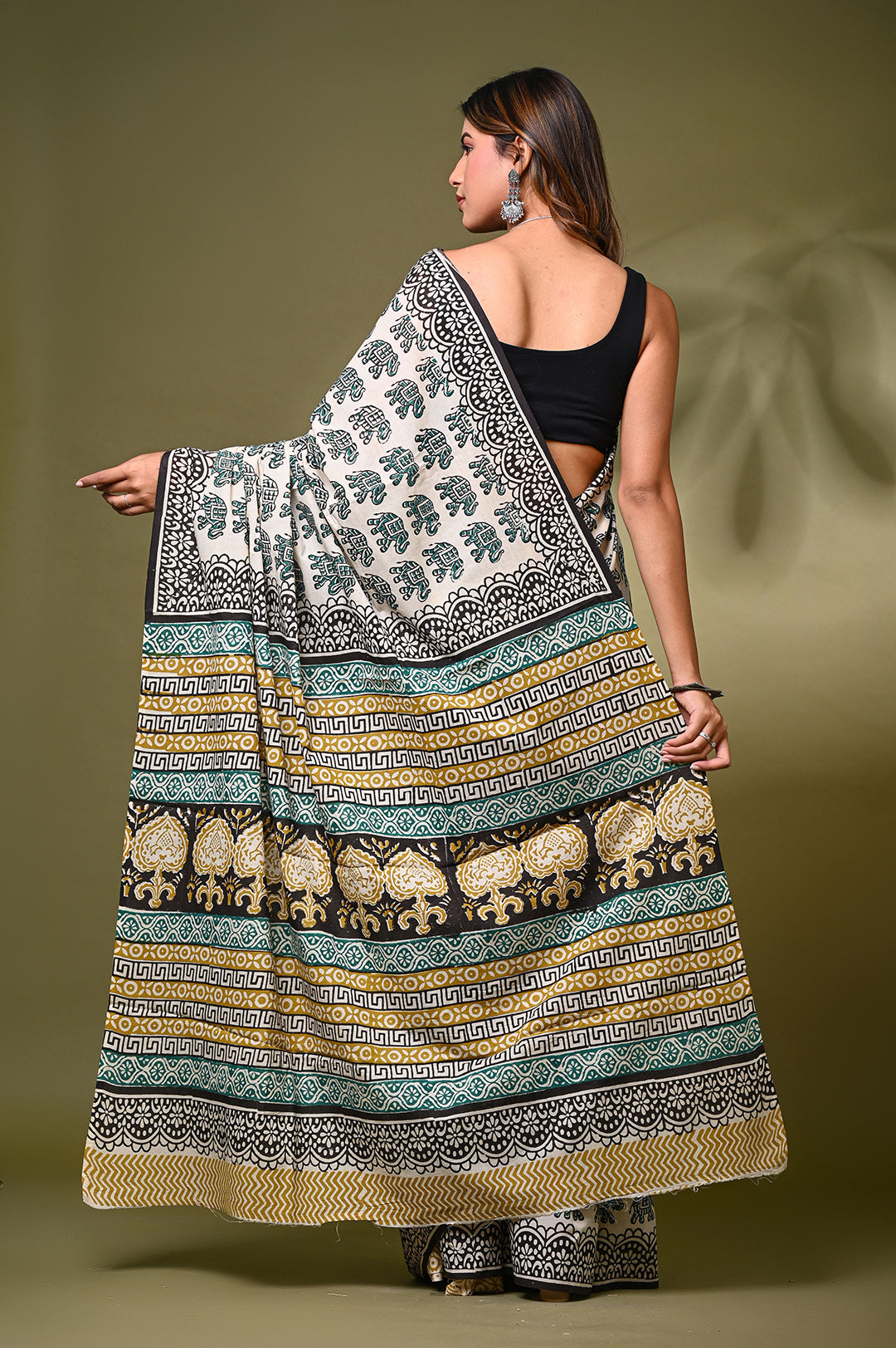 Back profile of a woman draping a lightweight Rajasthani block print cotton saree with traditional black ethnic motifs and a patterned pallu, paired with a black sleeveless blouse.