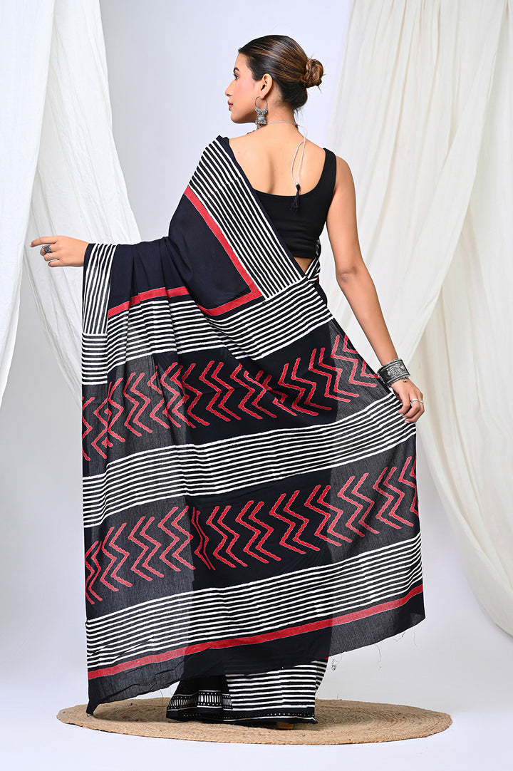 Full-length rear view of a model showcasing the detailed pallu of a plain black Bagru handblock print mulmul cotton saree, featuring crisp black and white stripes and red zigzag geometric motifs against a white backdrop.