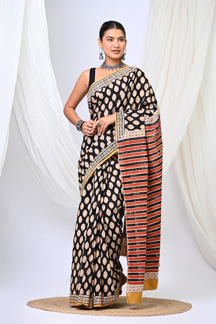 Front view of a model in an authentic black and beige Bagru handblock print mulmul cotton saree, featuring a delicate buti floral pattern and a rust-striped pallu.