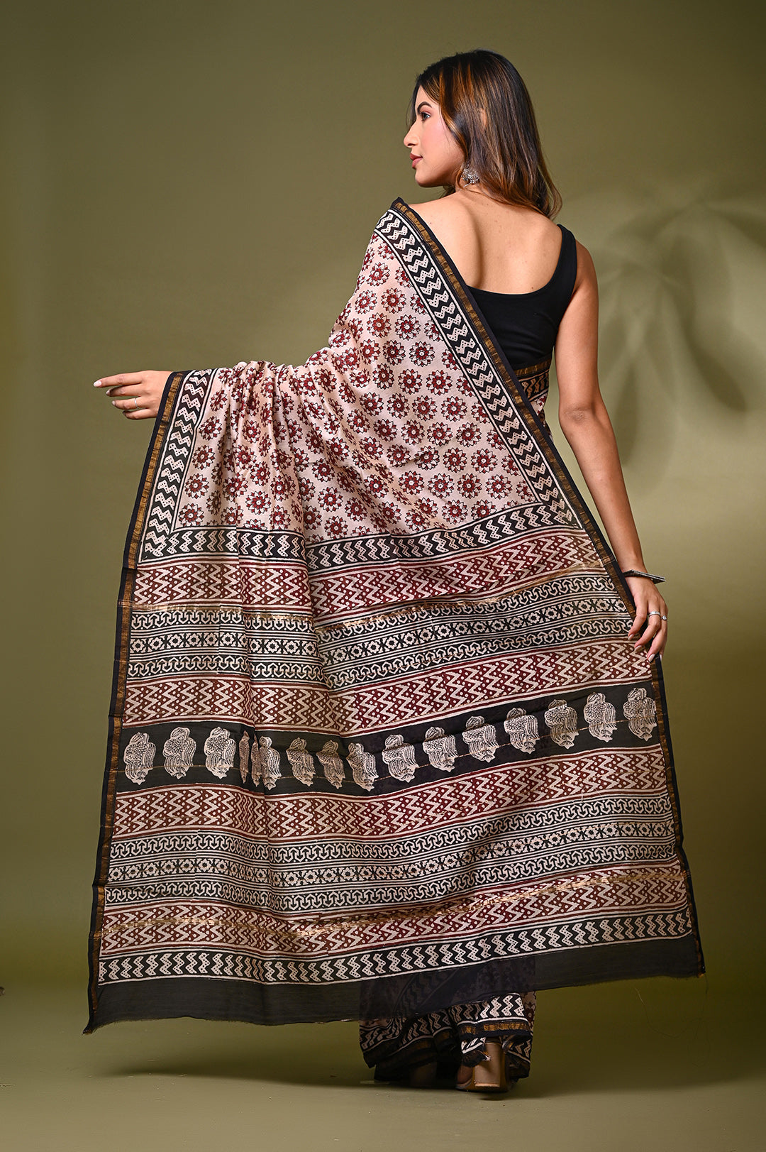 Back view of a woman modeling an authentic natural cream Chanderi silk saree, showcasing the elegant drape of its intricate black and rust Bagru block-printed patterns and elaborate traditional pallu border.