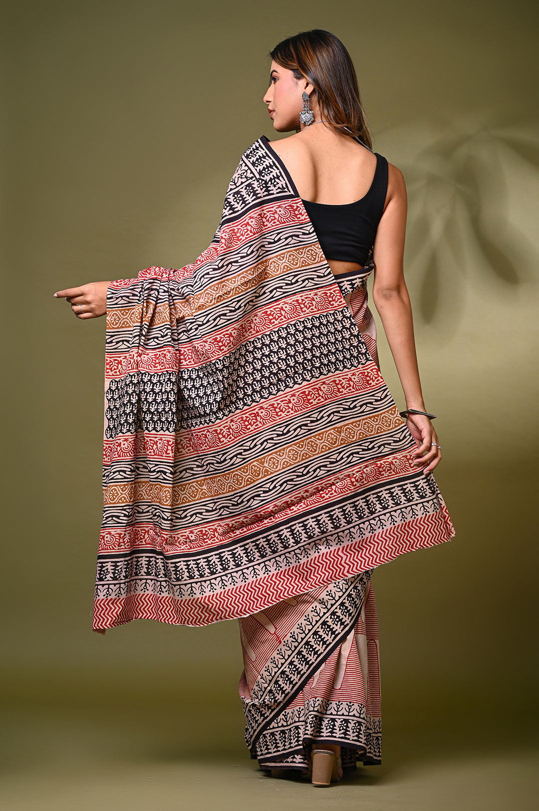 Rear view of a model showcasing the draped pallu of an off-white and cream Bagru handblock print mulmul cotton saree, featuring intricate black geometric motifs and maroon borders.