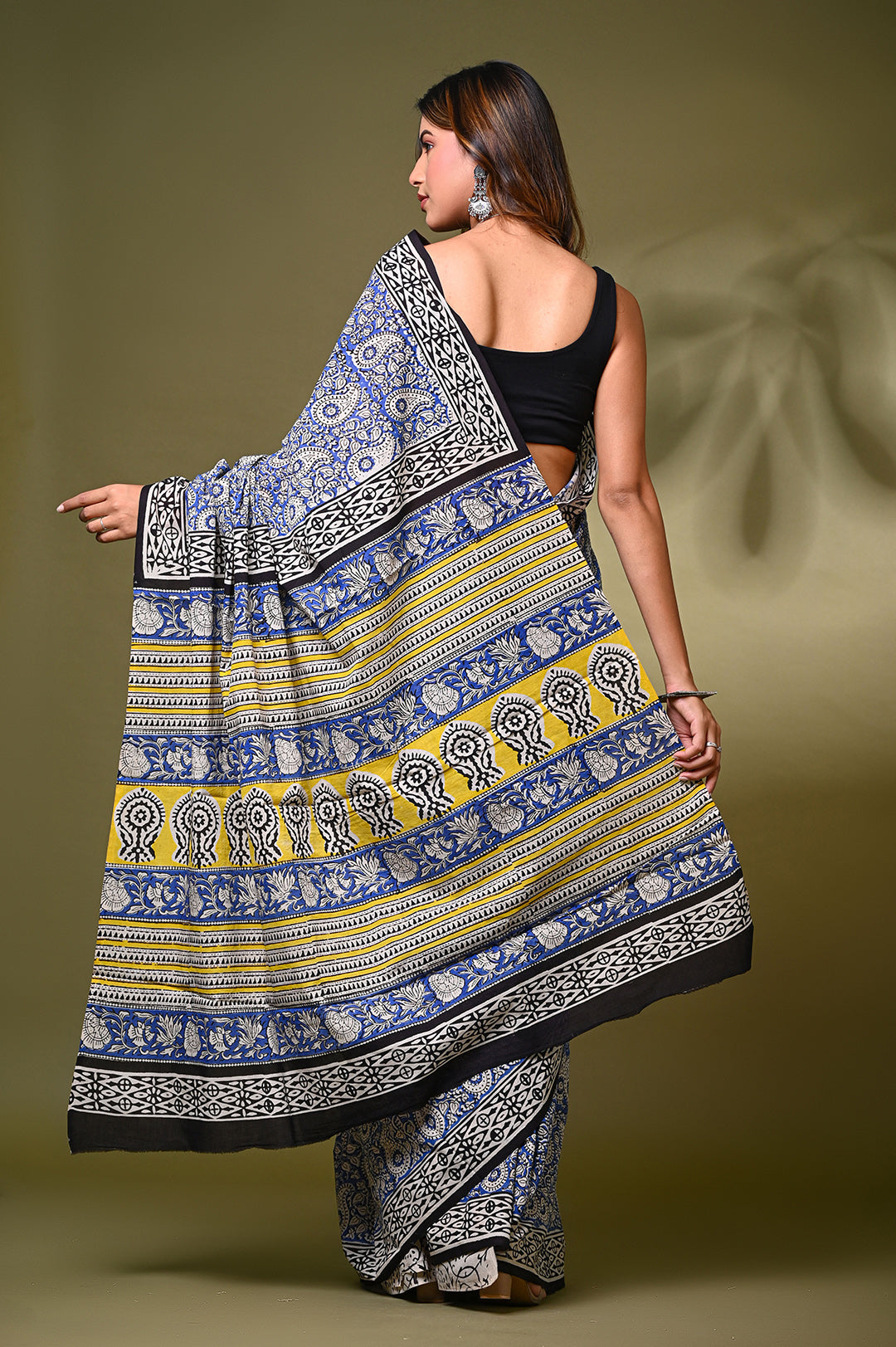 Back view of a model showcasing the detailed pallu of a Bagru handblock print mulmul cotton saree, featuring blue and off-white paisley patterns with a striking yellow geometric border.