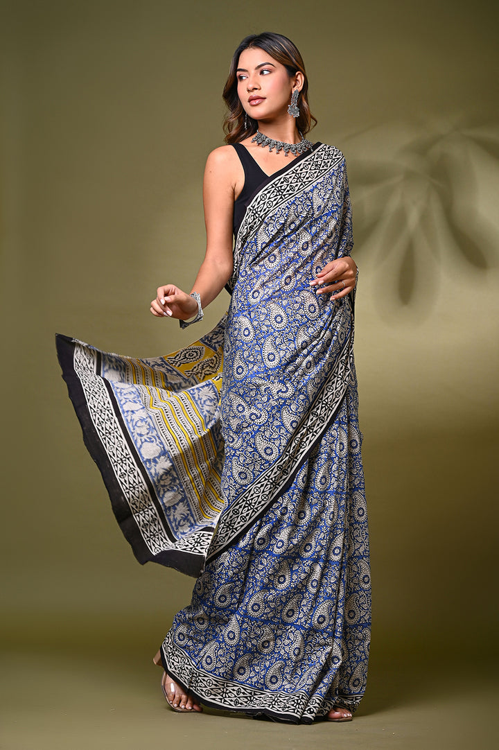 Full-length front view of a model in an authentic Bagru handblock printed blue and off-white mulmul cotton saree, showcasing a gracefully draped pallu with a bold yellow, black, and cream patterned border.