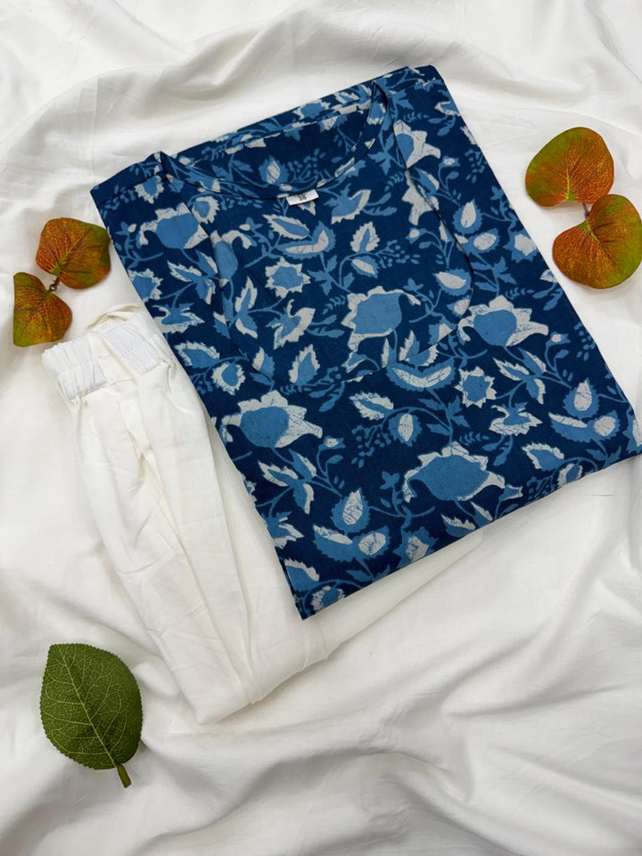 Deep Indigo Blue color ka authentic Bagru hand block print kurta aur matching white bottom trouser set, jo ek safed kapde par neatly fold karke rakha hua hai aur aaspaas decorative patte hain.
