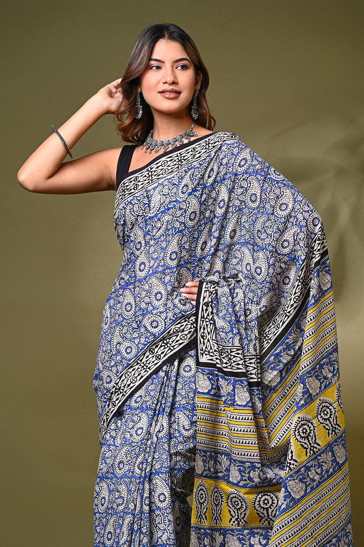 Full-length studio shot of a woman draping a traditional Rajasthani Bagru printed malmal saree featuring geometric borders, paired with a sleeveless black blouse against a soft olive background.
