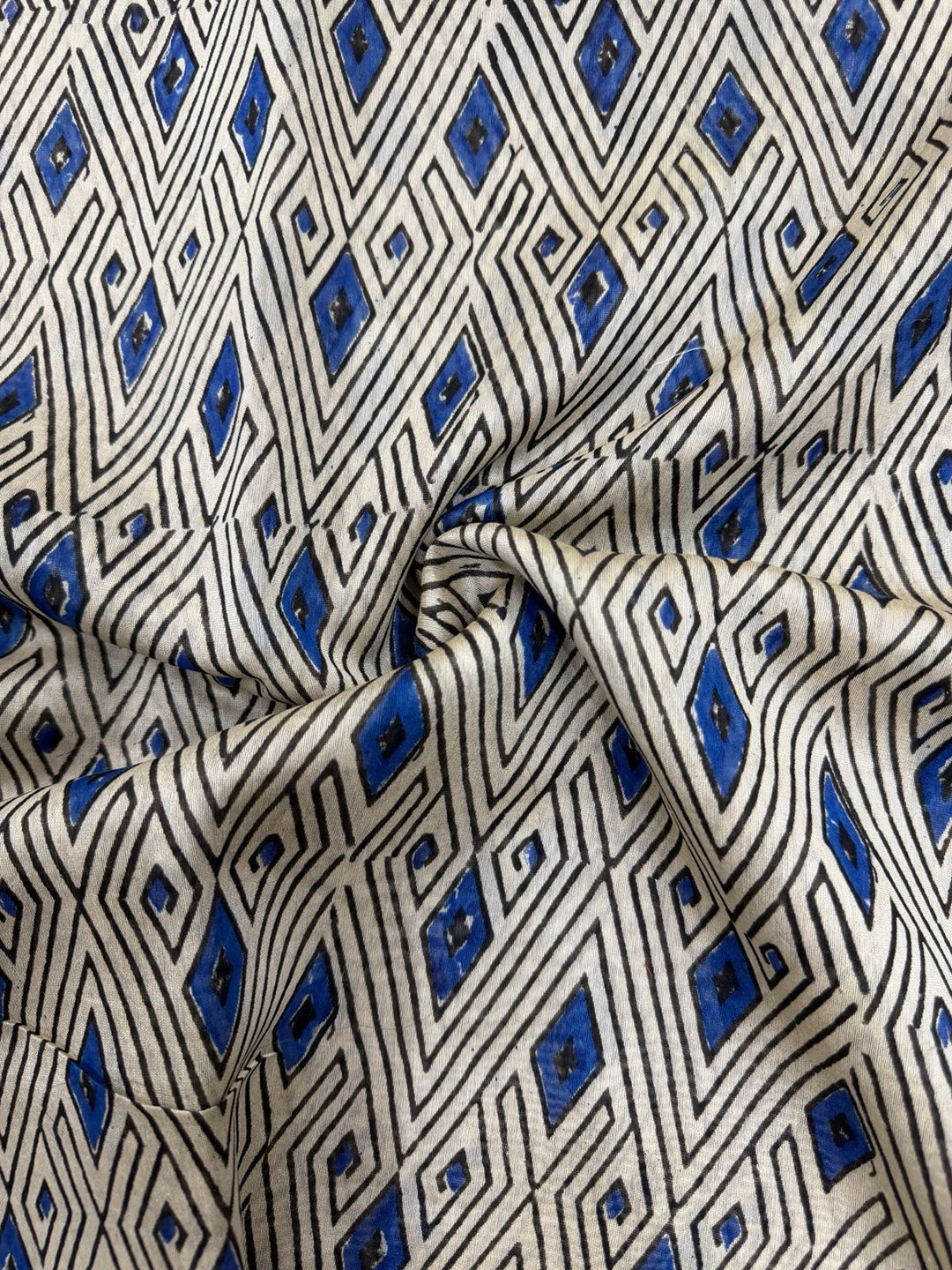 Fine detail of a sheer Chanderi Silk fabric featuring traditional Indian hand block prints in blue, black, and white with a zari-accented traditional border.