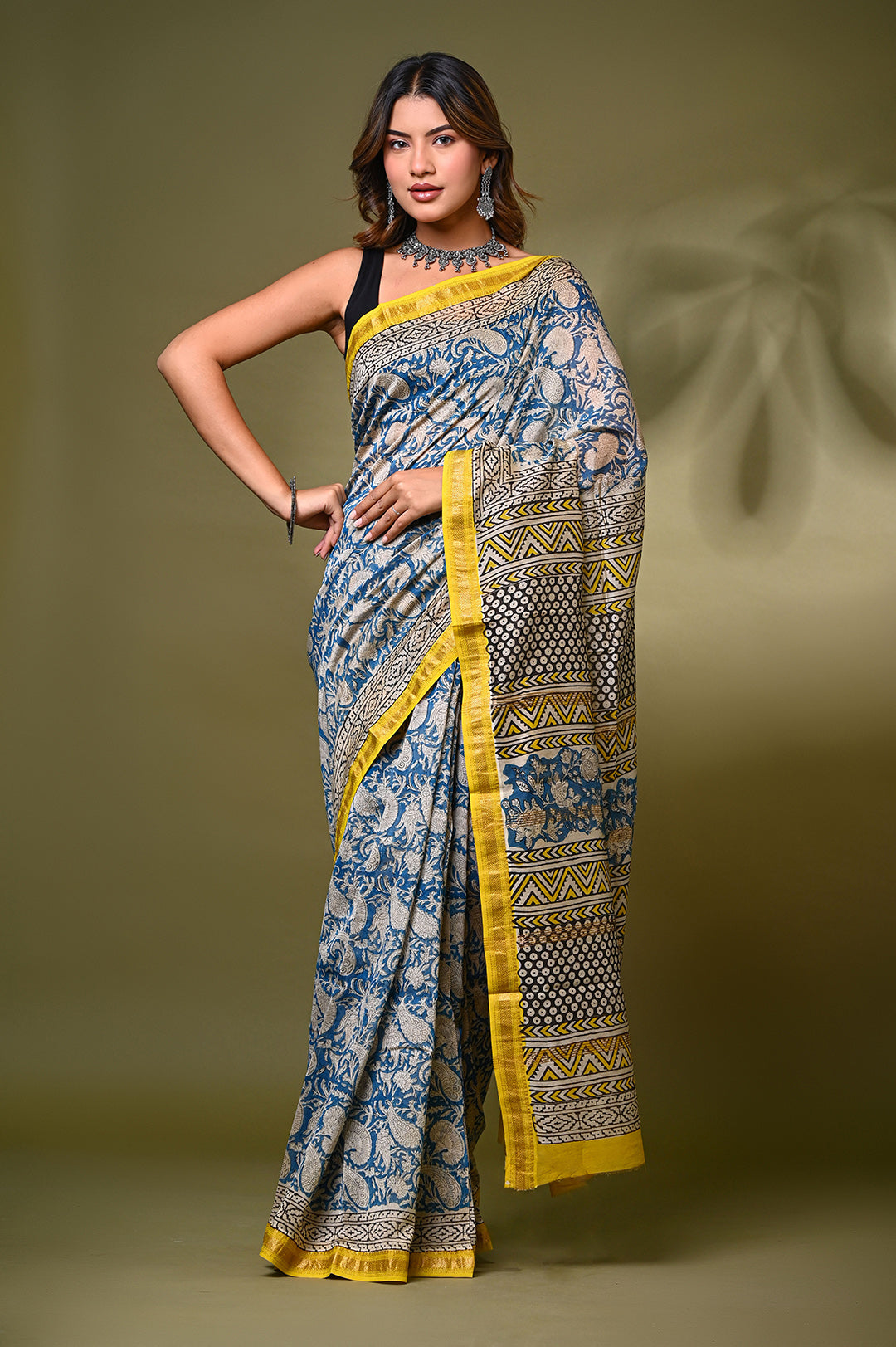 "A woman wearing a blue and cream Maheshwari silk saree with traditional Bagru hand-block floral prints and a striking yellow zari border.