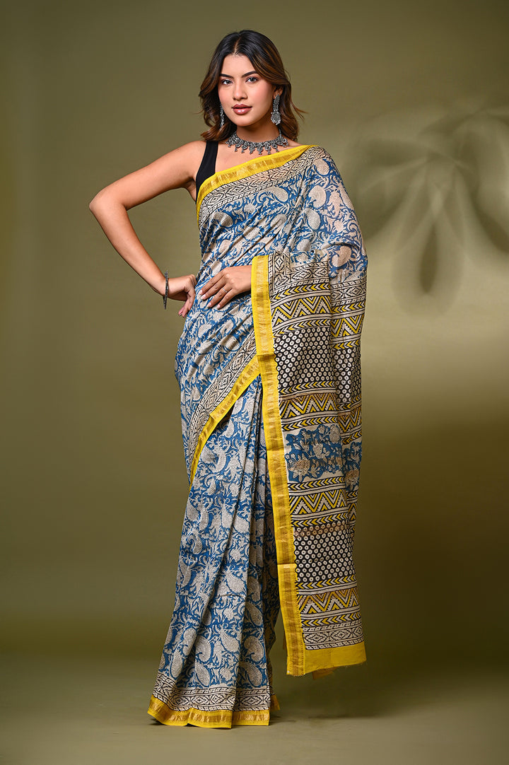 "A woman wearing a blue and cream Maheshwari silk saree with traditional Bagru hand-block floral prints and a striking yellow zari border.