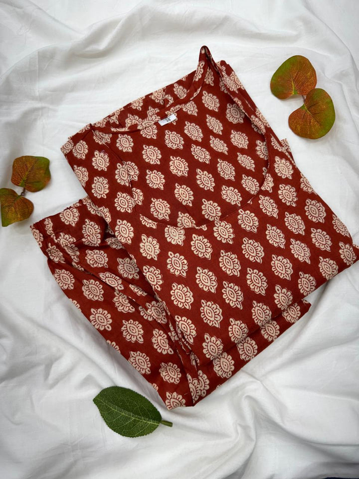 Rust Gud color ka Bagru hand block print top aur bottom co-ord set ek safed kapde par fold karke rakha hua hai, jisme traditional ethnic motifs bane hain.
