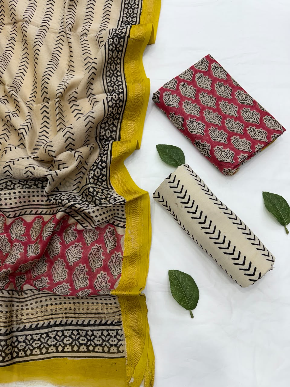 Full flat lay view of the Peach Bagru Traditional Buti Print Maheshwari Silk Suit Set, displaying a folded cream dupatta featuring fine black chevron and red floral motifs with a yellow Zari border, alongside the red and black floral block-printed kurta fabric, and a neatly rolled cream bottom fabric.
