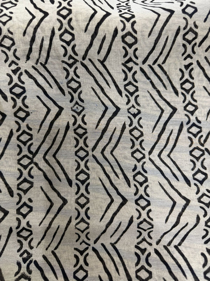Close-up detail of a Chanderi Silk saree featuring traditional black hand-block printed geometric patterns, zigzag lines, and circular motifs on a natural off-white background.