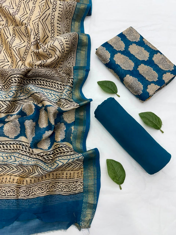 Full flat lay view of the Blue Traditional Bagru Hand Block Print Maheshwari Silk Suit Set, displaying a folded beige and blue patterned dupatta with a golden Zari border, a matching blue hand block-printed kurta fabric, and a neatly rolled solid deep blue bottom fabric styled with fresh green leaves.