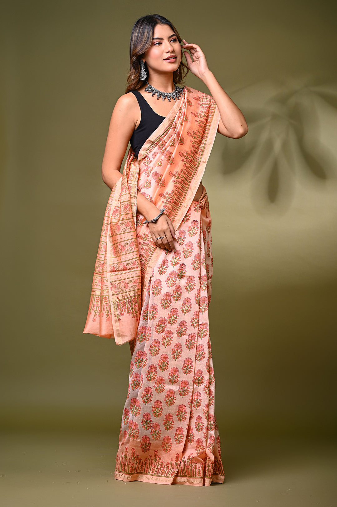 A woman posing in a blush peach Sanganeri handblock print Chanderi Silk saree, highlighting the lightweight shimmering drape, delicate red and green floral butis, and a detailed border.