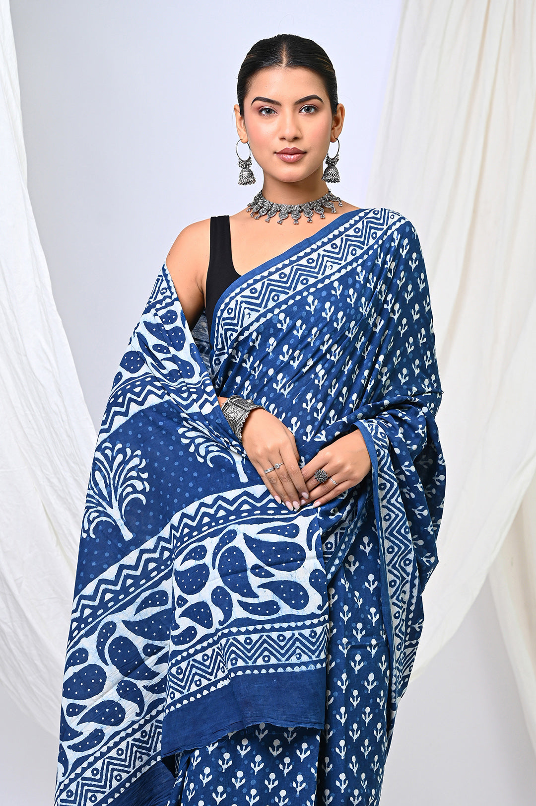 Close-up front view of a model draping a pure indigo blue Dabu handblock print mulmul cotton saree, showcasing the intricate white tree-of-life motifs and geometric borders on the pallu.