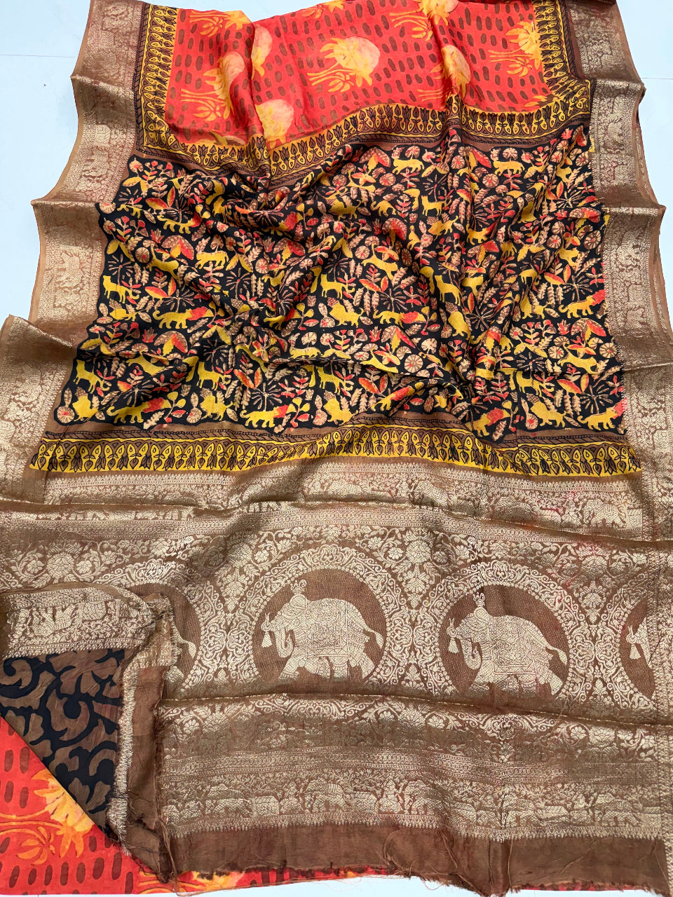 A traditional Indian Banarasi silk saree with a black body patterned with yellow and red floral motifs, featuring a brown zari border with elephant motifs and a red and gold pallu.