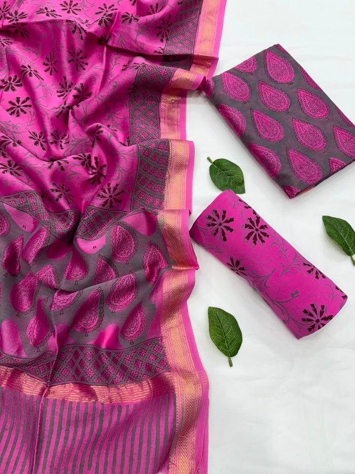 Full flat lay view of the Gulabi Pink Hand Block Print Maheshwari Silk Suit Set, displaying the charcoal grey patterned kurta fabric, a matching vibrant pink block-printed dupatta with a golden Zari border, and a neatly folded pink floral bottom fabric decorated with fresh green leaves.