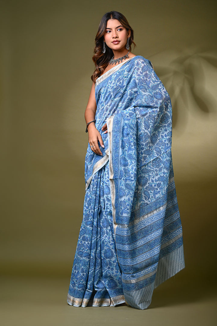Model wearing a light blue Sanganeri hand-block floral print Maheshwari silk-cotton saree with a classic gold zari border and matching unstitched blouse piece.