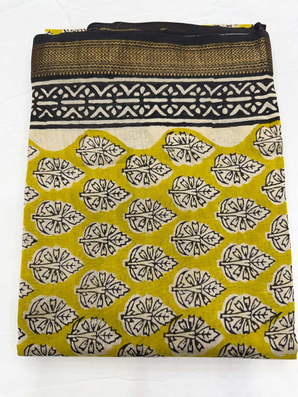Close-up of the unstitched warm mustard yellow Maheshwari silk kurta fabric, featuring traditional all-over black and cream Bagru hand block printed floral buti motifs.