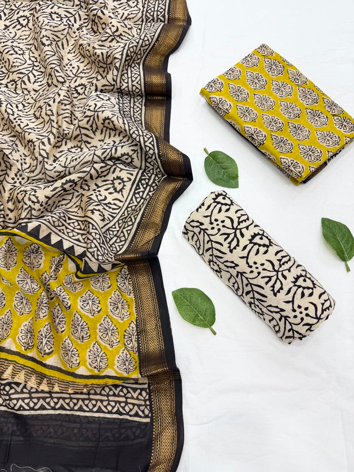 Full flat lay view of the Mustard Yellow Bagru Buti Print Maheshwari Silk Suit Set, displaying a vibrant mustard yellow kurta fabric with black and cream floral block prints, a matching cream dupatta with intricate black borders, and a neatly rolled cream patterned bottom fabric.
