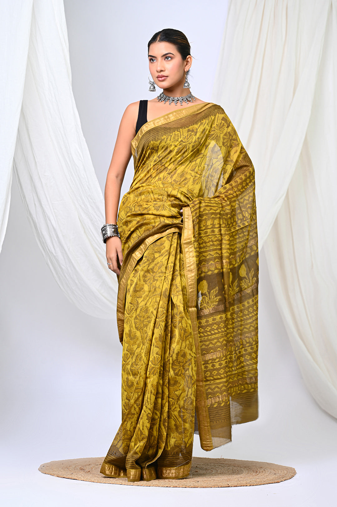 Premium natural mustard and yellow Maheshwari silk saree with a hand-stamped interlocking geometric pattern, styled against a soft white draped background.