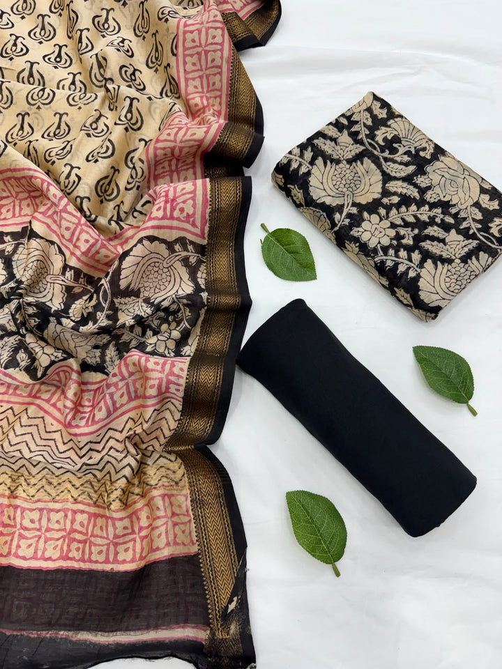 Full flat lay view of the Natural Black Bagru Print Maheshwari Silk Suit Set, displaying the black kurta fabric with golden floral motifs, a matching patterned dupatta with a golden Zari border, and a neatly rolled solid black bottom fabric styled with fresh green leaves.