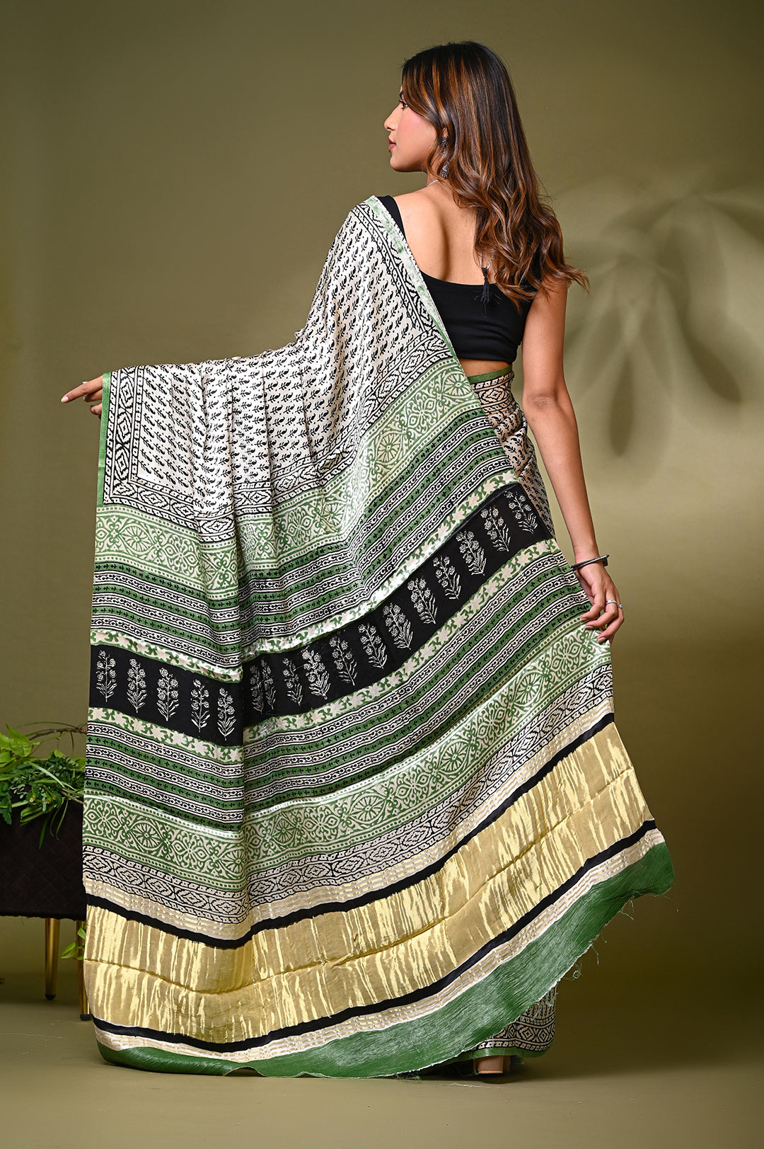 Side-angle view of a premium natural cream Modal Silk saree showcasing its glossy texture, fluid drape, and traditional Rajasthani block prints against an olive green background.