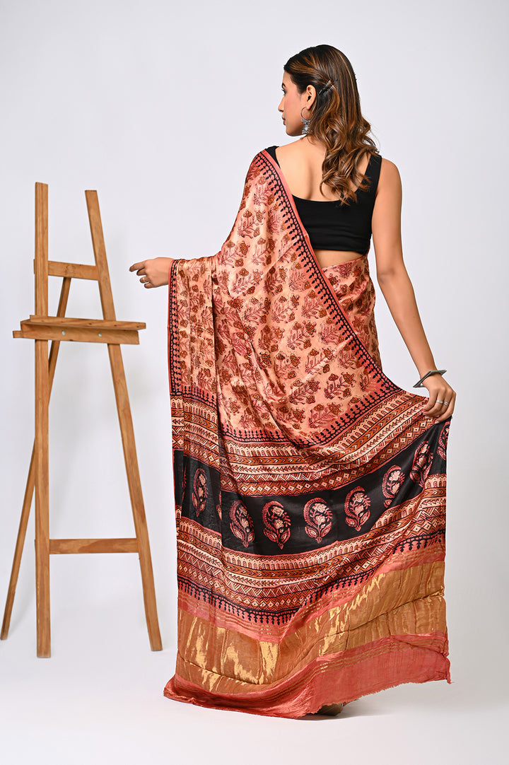 Side view of a premium natural red Modal Silk saree with traditional hand block printed motifs and a golden-accented pallu, styled elegantly next to a wooden artist easel.
