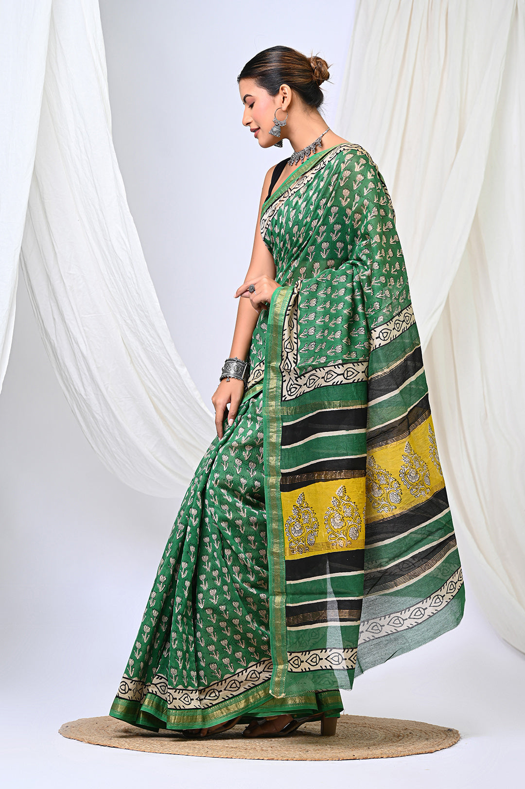 Side view of a woman elegant draping a natural green Maheshwari silk saree featuring traditional handblock printed buti motifs and an ornate geometric border.