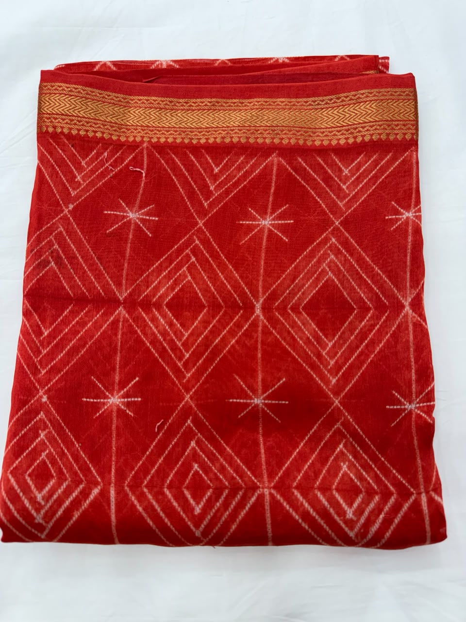 Close-up of the unstitched orange Maheshwari silk kurta fabric, highlighting the crisp white diamond patterns created through traditional hand-stitched and resist-dyed Shibori art.