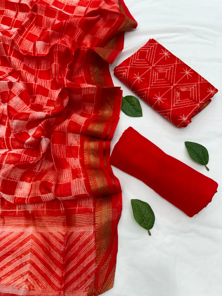 Full flat lay view of the Orange Stitching Shibori Art Maheshwari Silk Suit Set, showcasing the red-orange geometric shibori kurta fabric, matching patterned dupatta with a golden handloom woven Zari border, and a neatly rolled solid orange bottom fabric decorated with fresh green leaves.