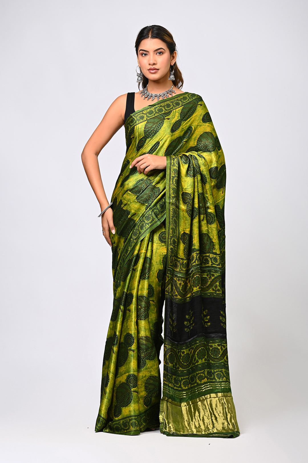 A woman modeling a natural green Modal Silk saree dyed with pomegranate rind, featuring black Ajrakh block prints by Bagru Hastkala Printers.